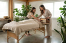 A professional sound healing instructor demonstrating how to use a vibroacoustic therapy amplifier and massage table to a student in a serene wellness studio.