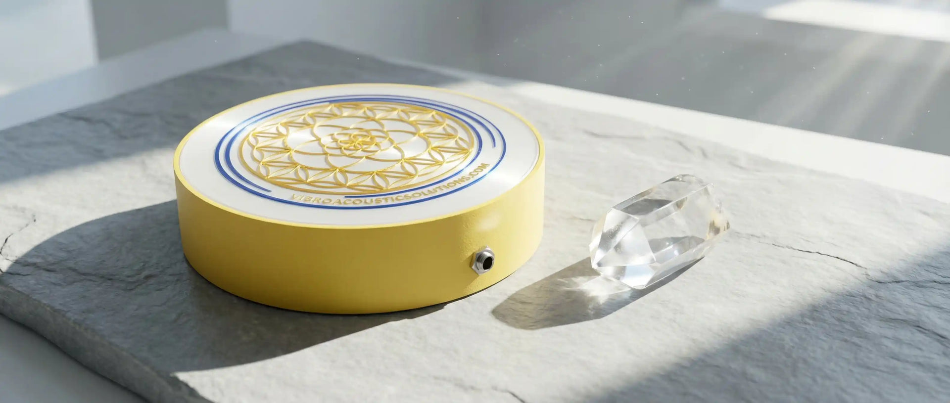 A sleek vibroacoustic transducer and a clear quartz crystal resting in bright sunlight, representing clarity and answers for sound therapy equipment.